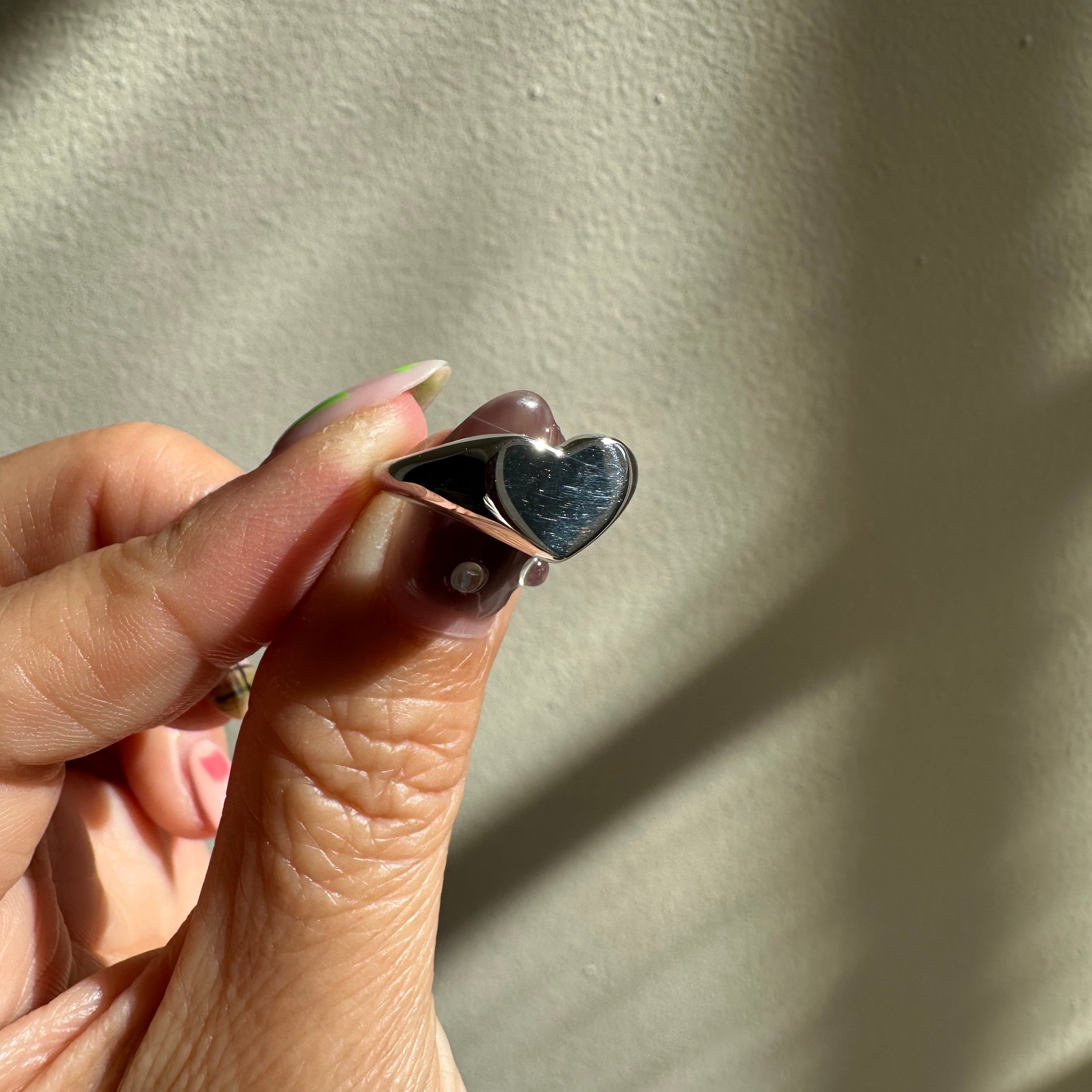 Heart-shaped silver ring held between fingers on a neutral background